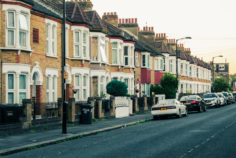 A row of terraced homes on Euston Road featuring diverse exterior facades in white, beige, and brick-red, with some buildings displaying decorative brickwork. The gardens in front of the houses are we